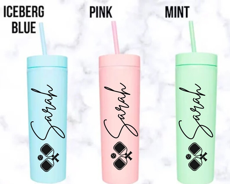 K&ouml;nnte beinhalten: Drei personalisierte Becher mit einem Pickleball-Design. Die Becher sind in den Farben Eisblau, Pink und Mint. Jeder Becher tr&auml;gt den Namen "Sarah" aufgedruckt.