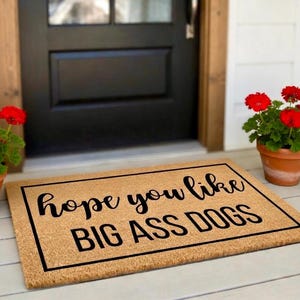 Peut inclure: Un paillasson rectangulaire en fibre de coco beige avec une bordure noire et le texte noir "hope you like BIG ASS DOGS" imprim&eacute; au centre. Le tapis pr&eacute;sente une police cursive pour la premi&egrave;re ligne et une police grasse pour la seconde.