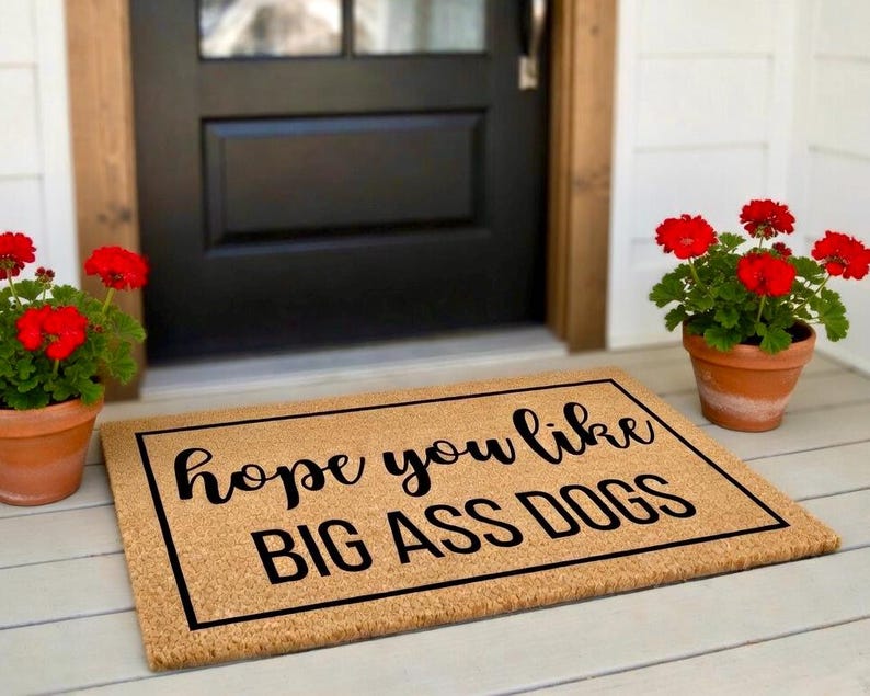 Peut inclure: Un paillasson rectangulaire en fibre de coco beige avec une bordure noire et le texte noir "hope you like BIG ASS DOGS" imprim&eacute; au centre. Le tapis pr&eacute;sente une police cursive pour la premi&egrave;re ligne et une police grasse pour la seconde.