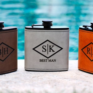 May include: Three personalized leather flasks with different initials and the text "Best Man" on one flask. The flasks are brown, gray, and orange.