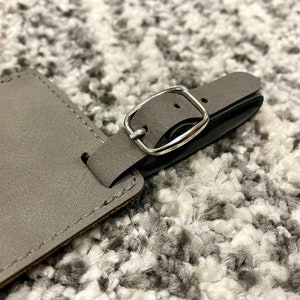 Peut inclure: Une &eacute;tiquette &agrave; bagages en cuir gris avec une boucle en m&eacute;tal argent&eacute;. L'&eacute;tiquette est cousue sur les bords.