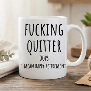 Peut inclure: Mug en céramique blanche avec l'inscription noire "FUCKING QUITTER", suivie de "OOPS" et "I MEAN HAPPY RETIREMENT". La tasse a une anse incurvée et est probablement utilisée pour les boissons. Un cadeau humoristique pour un retraité.