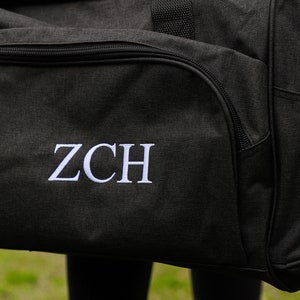 May include: Black duffel bag with a white embroidered monogram "ZCH" and a silver zipper pull with the word "dalix" on it.