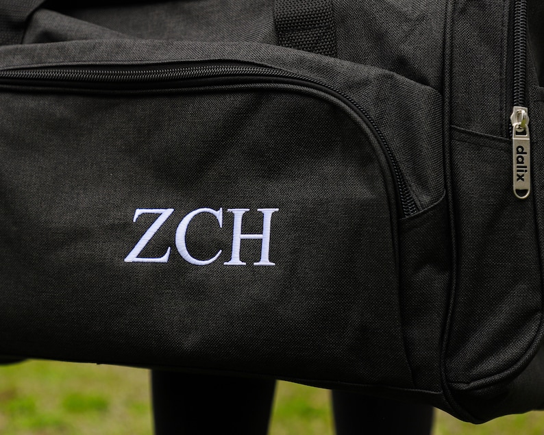 May include: Black duffel bag with a white embroidered monogram "ZCH" and a silver zipper pull with the word "dalix" on it.