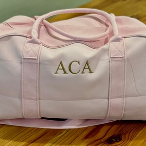 May include: A pink canvas duffel bag with gold embroidered initials "ACA".