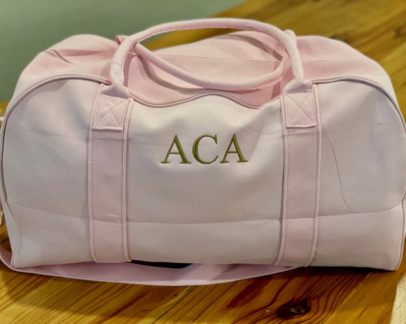 May include: A pink canvas duffel bag with gold embroidered initials "ACA".