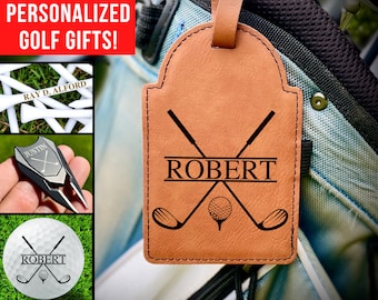 May include: Personalized leather golf bag tag with a brown background and black text. The tag features a golf ball and two crossed golf clubs with the name "ROBERT" printed on the tag.