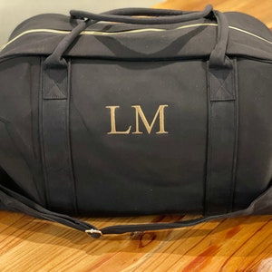 May include: Black canvas duffel bag with gold zipper accents and a gold embroidered monogram "LM".