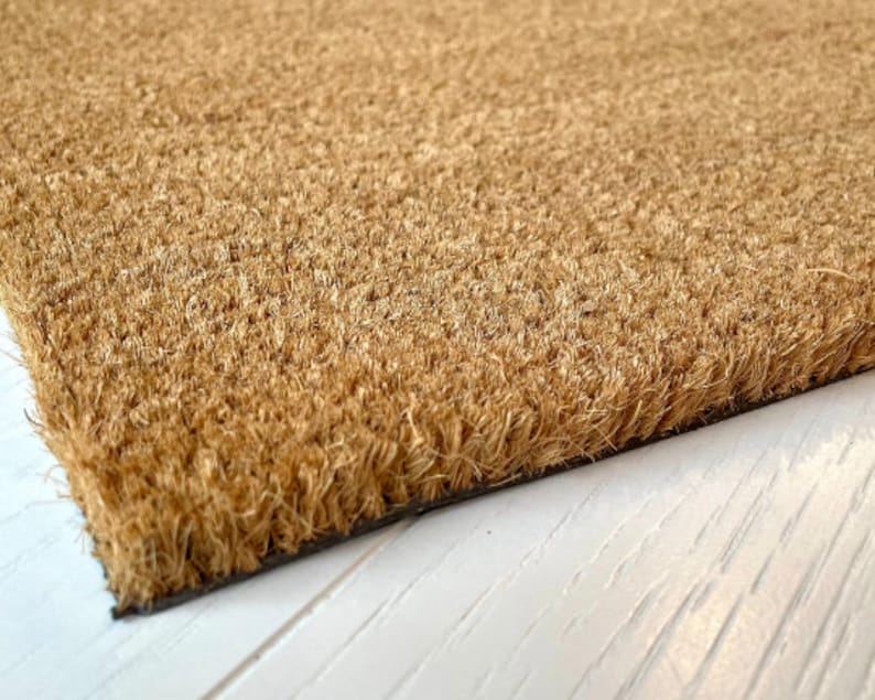 Peut inclure: Un paillasson rectangulaire en fibres de coco marron naturel. Le tapis a une bordure fonc&eacute;e et une surface textur&eacute;e, adapt&eacute;e &agrave; une utilisation en ext&eacute;rieur. Les fibres de coco sont dens&eacute;ment tass&eacute;es, cr&eacute;ant une surface durable et efficace pour essuyer les chaussures.