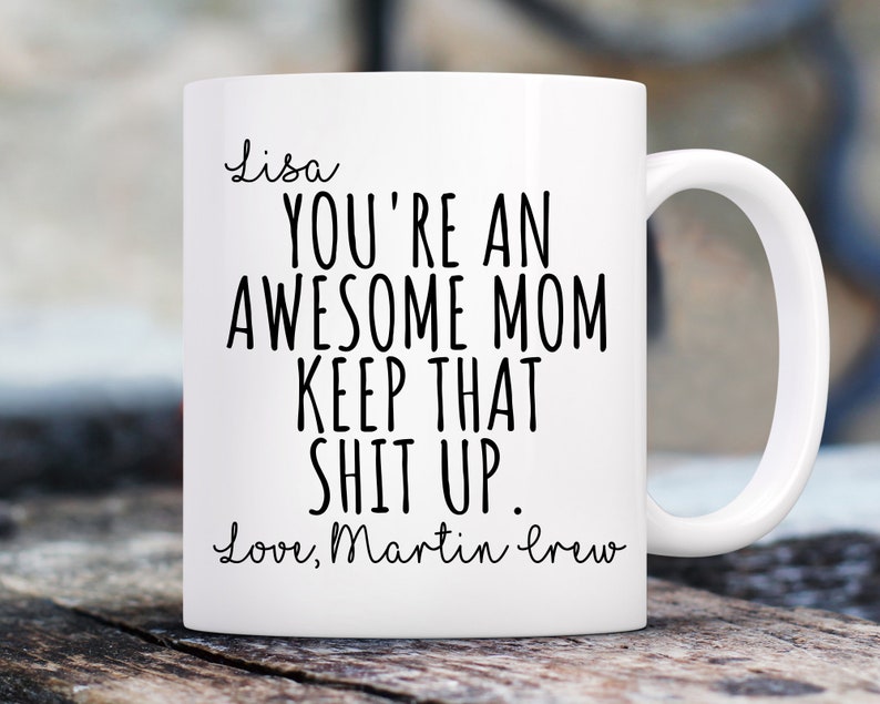 May include: White ceramic mug with a curved handle. The mug features black text that reads "Lisa, YOU'RE AN AWESOME MOM KEEP THAT SHIT UP. Love, Martin crew."