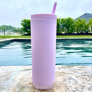 May include: A light pink stainless steel tumbler with a lid and a pink straw. The tumbler is sitting on a stone surface next to a swimming pool.