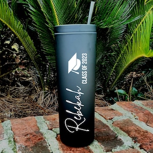 Puede incluir: Vaso de acero inoxidable negro con un gorro de graduaci&oacute;n blanco y el texto "Class of 2023" y el nombre "Rebekah" en una fuente cursiva.