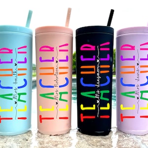 May include: Four colourful stainless steel tumblers with straws. Each tumbler has the word "TEACHER" written in rainbow colours with a teacher's name underneath. The tumblers are in blue, pink, black, and purple.