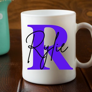 May include: White ceramic mug with a large purple letter "R" and the name "Rylie" written in black cursive script.