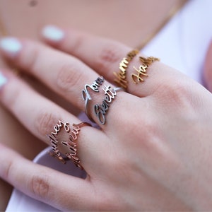 May include: Three gold rings with names engraved on them. The rings are worn on a person's finger. The names on the rings are "Hannah Hall", "Mama Bennett", and "Matthew Andrew".