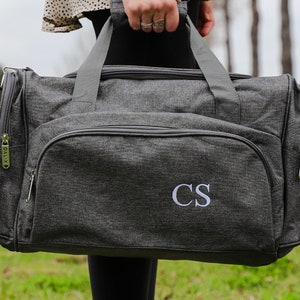 May include: A gray travel duffel bag with a zipper closure and a monogrammed "CS" on the front.