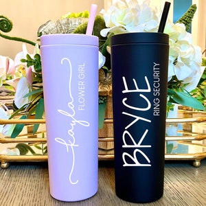 May include: Two insulated tumblers, one lavender and one black, with straws. The lavender tumbler has the name "Kayla" and "Flower Girl" in white script. The black tumbler has the name "Bryce" and "Ring Security" in white script.