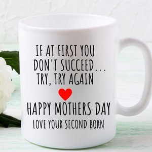 Może przedstawiać: Biały kubek ceramiczny z czarnym tekstem, kt&oacute;ry brzmi "IF AT FIRST YOU DON'T SUCCEED... TRY, TRY AGAIN" z czerwonym sercem i "HAPPY MOTHERS DAY LOVE YOUR SECOND BORN".