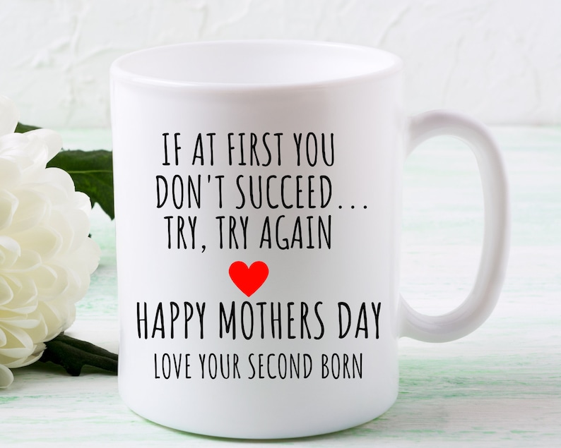 Może przedstawiać: Biały kubek ceramiczny z czarnym tekstem, kt&oacute;ry brzmi "IF AT FIRST YOU DON'T SUCCEED... TRY, TRY AGAIN" z czerwonym sercem i "HAPPY MOTHERS DAY LOVE YOUR SECOND BORN".