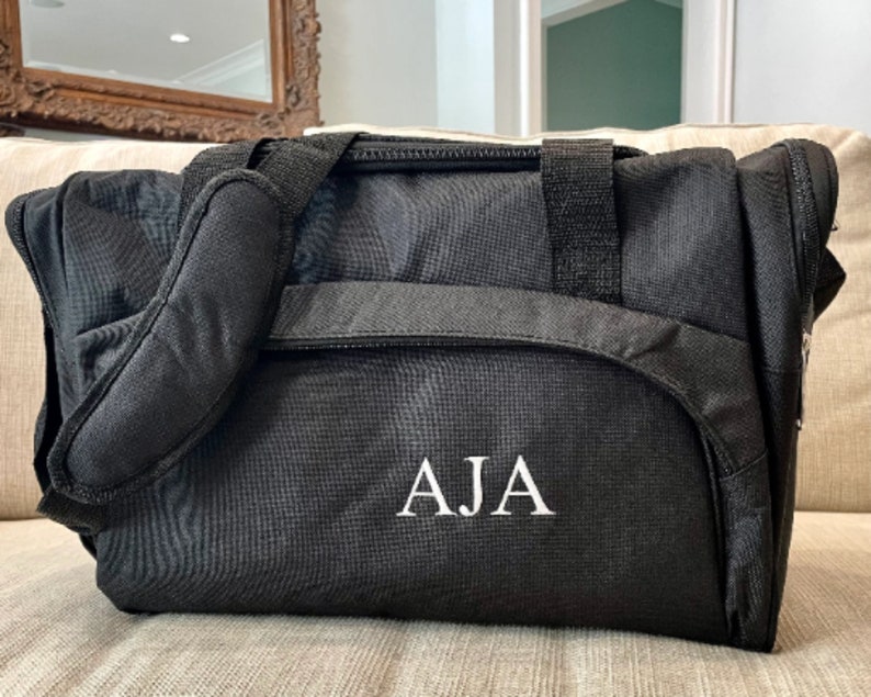 May include: Black travel duffel bag with a white embroidered monogram "AJA".