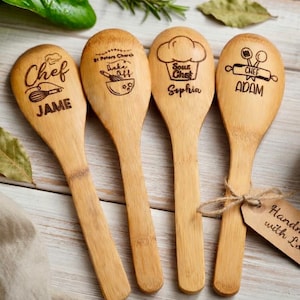 May include: Four wooden spoons with engraved text and illustrations. Each spoon features a different design: "Chef JAME", "St Peters Church Bake Off", "Sous Chef Sophia", and "Chef ADAM". The spoons are tied together with twine and a tag.