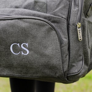 May include: Gray travel duffel bag with a zipper and a white embroidered monogram "CS" on the front.
