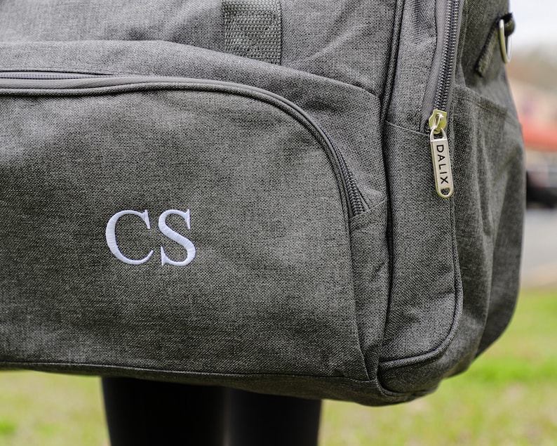 May include: Gray travel duffel bag with a zipper and a white embroidered monogram "CS" on the front.