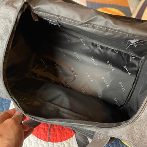 May include: A gray duffel bag with a black zipper and a black lining. The lining has the word "DALIX" printed on it repeatedly.