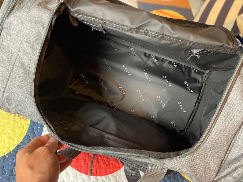 May include: A gray duffel bag with a black zipper and a black lining. The lining has the word "DALIX" printed on it repeatedly.