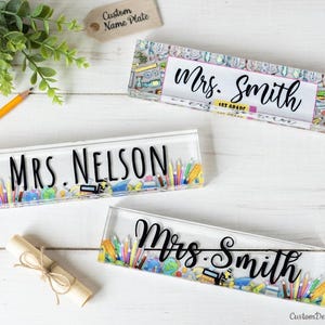 May include: Clear acrylic desk name plates with black lettering. The name plates read "Mrs. Smith" and "Mrs. Nelson". The name plates are decorated with colorful school supplies and the text "1st Grade".