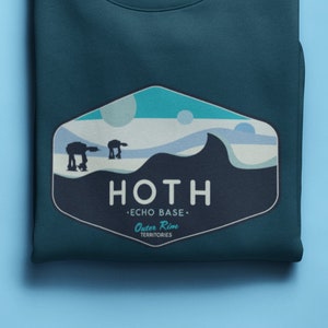 May include: A dark blue sweatshirt with a graphic of a Star Wars scene from the planet Hoth. The graphic features two AT-AT walkers walking across a snowy landscape. The text "Hoth - Echo Base - Outer Rim Territories" is printed below the graphic.