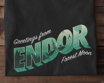 May include: Black t-shirt with a green and white graphic that says "Greetings from Endor Forest Moon".
