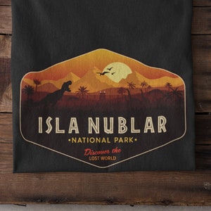 May include: Black t-shirt with a graphic of a sunset over a jungle with a dinosaur and the text "Isla Nublar National Park. Discover the Lost World."