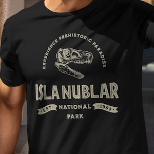 May include: Black t-shirt with a white graphic of a dinosaur skull and the text "Experience Prehistoric Paradise Isla Nublar National Park Est. 1993."