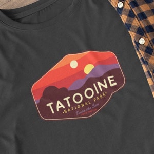 May include: Black long-sleeve t-shirt with a vintage-style national park logo featuring a sunset landscape and the text "Tatooine National Park - Twin suns of Tatooine"