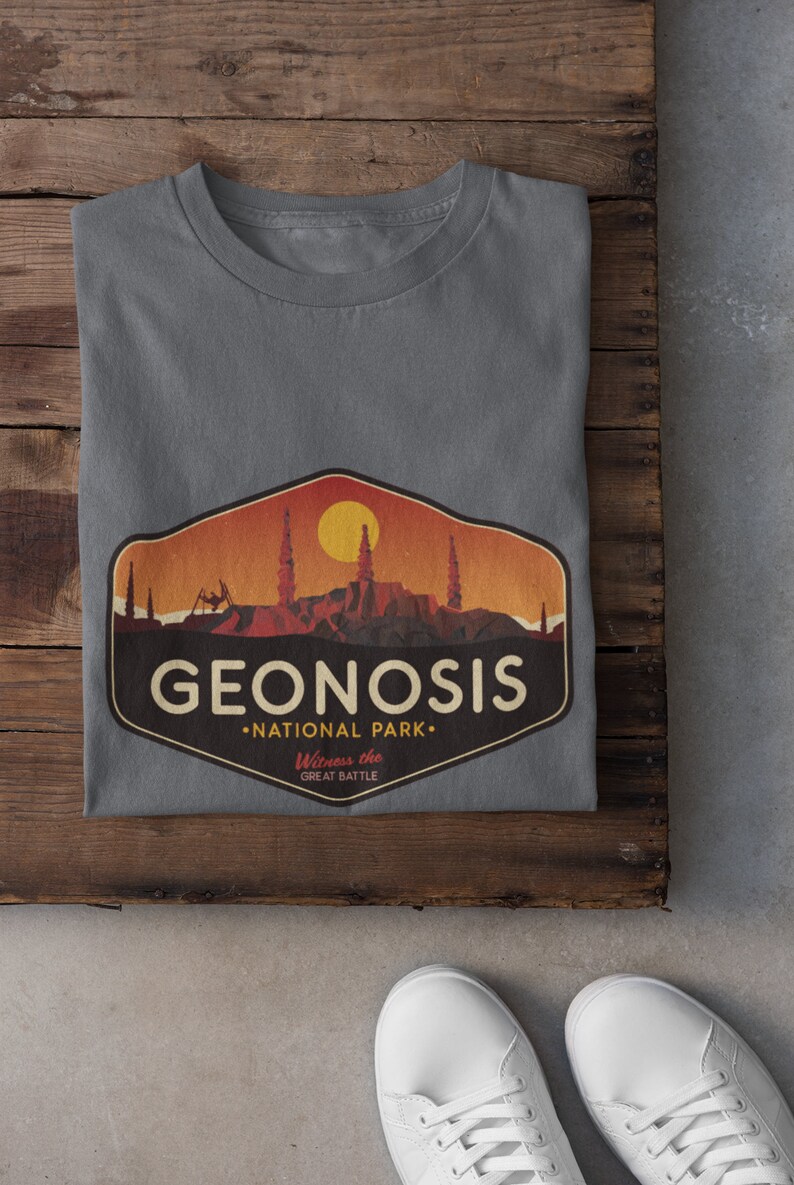 May include: A grey t-shirt featuring a vintage-style graphic of the fictional planet Geonosis from Star Wars. The graphic depicts a sunset over a rocky landscape with the text "Geonosis National Park. Witness the Great Battle."