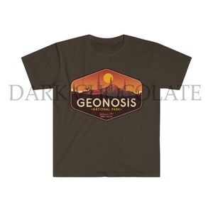 May include: A brown t-shirt featuring a vintage-style graphic of the fictional planet Geonosis from Star Wars. The graphic depicts a cityscape and the text "Geonosis - National Park - Welcome to the Great Battle".