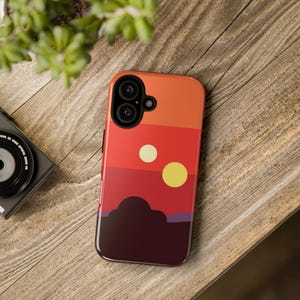 Op de afbeelding: Een zwarte telefoonhoes met een rood, oranje en geel zonsondergangsontwerp. De hoes heeft een silhouet van een planeet met twee manen aan de hemel.