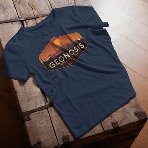 May include: A navy blue t-shirt featuring a vintage-style logo for Geonosis National Park. The logo depicts a sunset scene with a cityscape and the text "Geonosis National Park".
