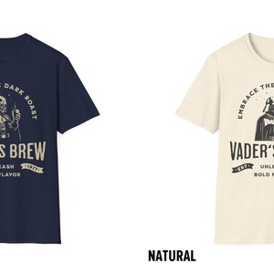May include: A navy blue and a natural colored t-shirt with a graphic of Darth Vader holding a cup of coffee. The text on the shirt reads "Embrace the Dark Roast, Vader's Brew, Est. 1977, Unleash Bold Flavor".