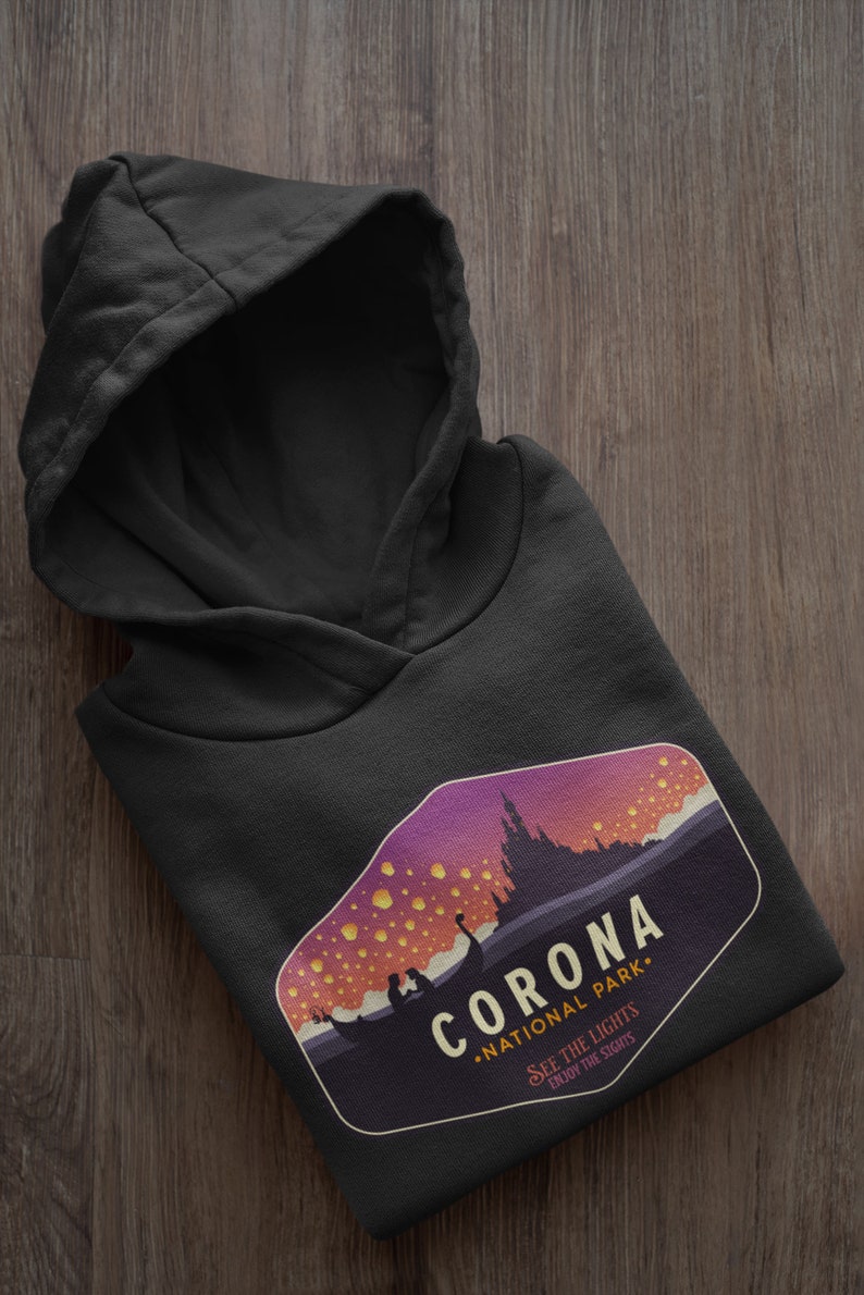 Puede incluir: Sudadera con capucha negra con un dise&ntilde;o gr&aacute;fico. El dise&ntilde;o presenta el texto "CORONA NATIONAL PARK" y una ilustraci&oacute;n de paisaje con linternas flotantes. El dise&ntilde;o incluye las frases "SEE THE LIGHTS" y "ENJOY THE SIGHTS".