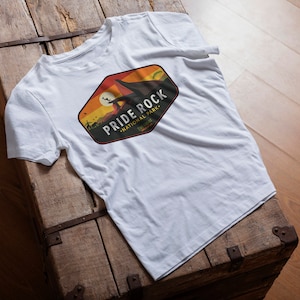 May include: White t-shirt with a colorful graphic design of a national park logo. The logo says "Pride Rock National Park, Telluride".
