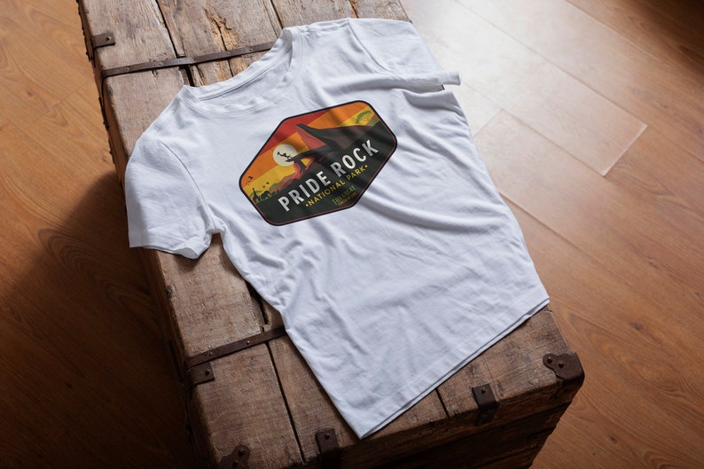 May include: White t-shirt with a colorful graphic design of a national park logo. The logo says "Pride Rock National Park, Telluride".