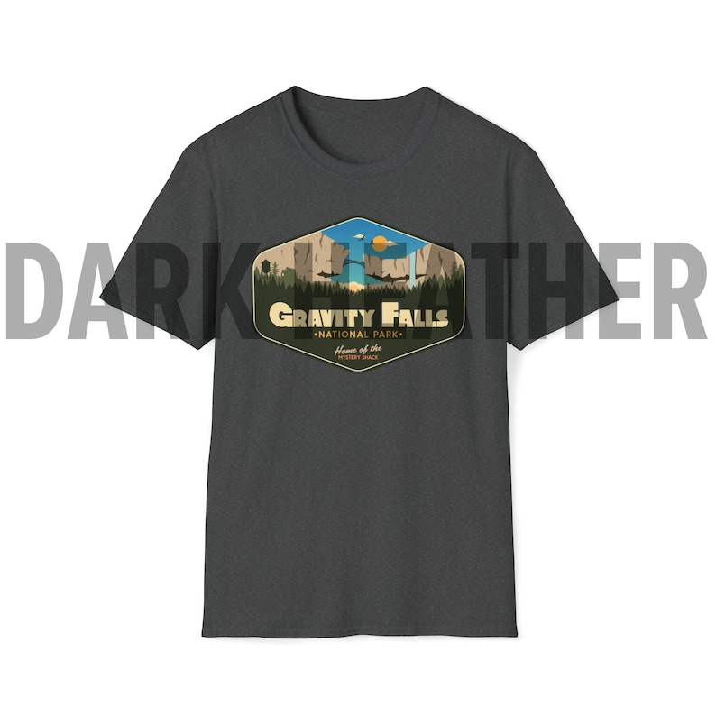 K&ouml;nnte beinhalten: Dunkelgraues T-Shirt mit einem Aufdruck des Gravity Falls National Park Logos. Das Logo zeigt ein stilisiertes Bild eines Wasserfalls, Bergen und B&auml;umen. Der Text "Gravity Falls National Park" ist in einer Vintage-Schriftart geschrieben. Der Text "Home of the Mystery Shack" ist in einer kleineren Schriftart unter dem Haupttext geschrieben.