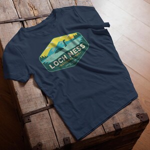 May include: A navy blue t-shirt with a green, yellow, and blue graphic of a Loch Ness Monster in a lake. The graphic says "Loch Ness National Park".