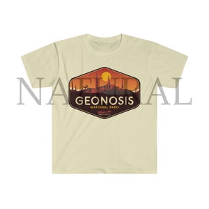May include: A beige t-shirt featuring a vintage-style graphic of a sunset over a cityscape. The graphic reads "Geonosis National Park" and "Welcome to the Great Battle".