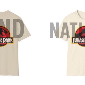 May include: Two t-shirts, one sand-colored and one natural-colored, each featuring the Jurassic Park logo. The logo includes a red circle with a dinosaur silhouette, the words "JURASSIC PARK" in white, and a yellow border.