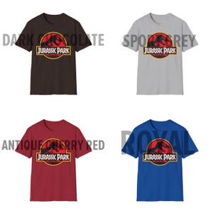 May include: Four short-sleeved t-shirts in dark chocolate, sport grey, antique cherry red, and royal blue. Each shirt features the Jurassic Park logo in a red circle with a yellow border. The text "JURASSIC PARK" is below the logo.
