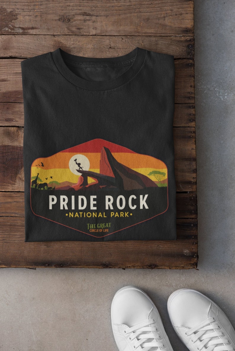 May include: Black t-shirt with a graphic of Pride Rock from The Lion King. The graphic features a sunset, a lion, and the text "Pride Rock National Park" with the tagline "The Great Circle of Life".