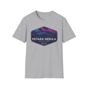 May include: A light gray t-shirt featuring a graphic of the Mutara Nebula National Park. The graphic is a dark blue, purple, and pink design inside a dark blue hexagon shape. The text "MUTARA NEBULA" is above "NATIONAL PARK".